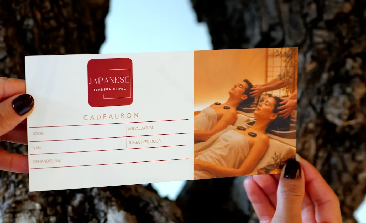 De cadeaubon van Japanese Headspa Clinic: rode kaart met logo, invulvelden en een foto van een duo-behandeling met hot stones